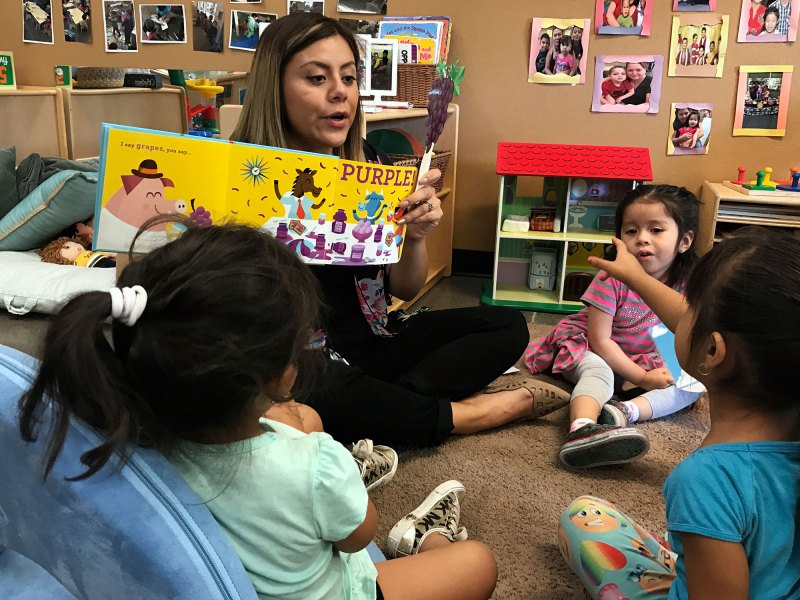 Angelina Salgado, a toddler room teacher, reads a book about colors aloud in the toddler room at the Phoenix, Ariz., branch of a model program for young children called Educare. Most state child care regulations do not require educational activities like reading aloud.