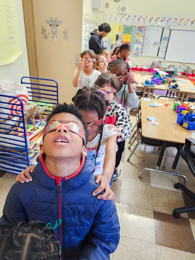 Little kids lined up, wearing glasses for the solar eclipse. 