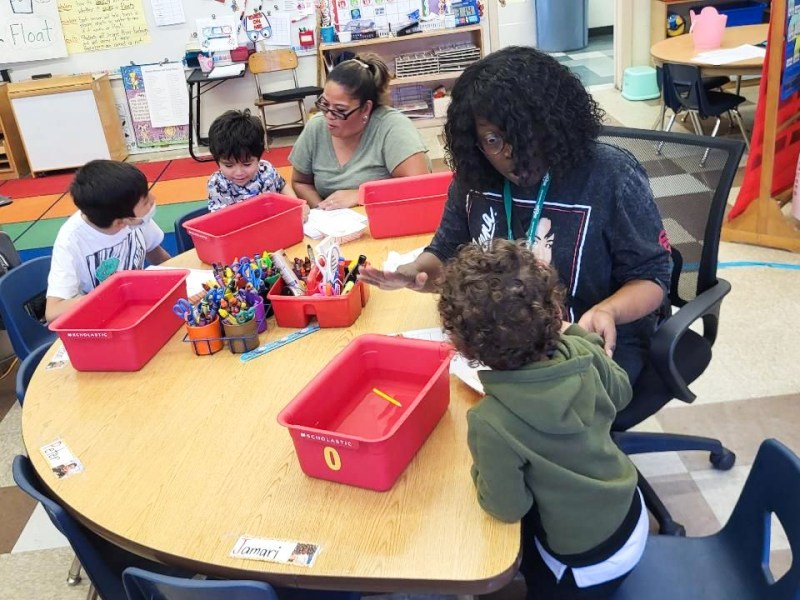 Kindergarteners work with two teachers around a circle table