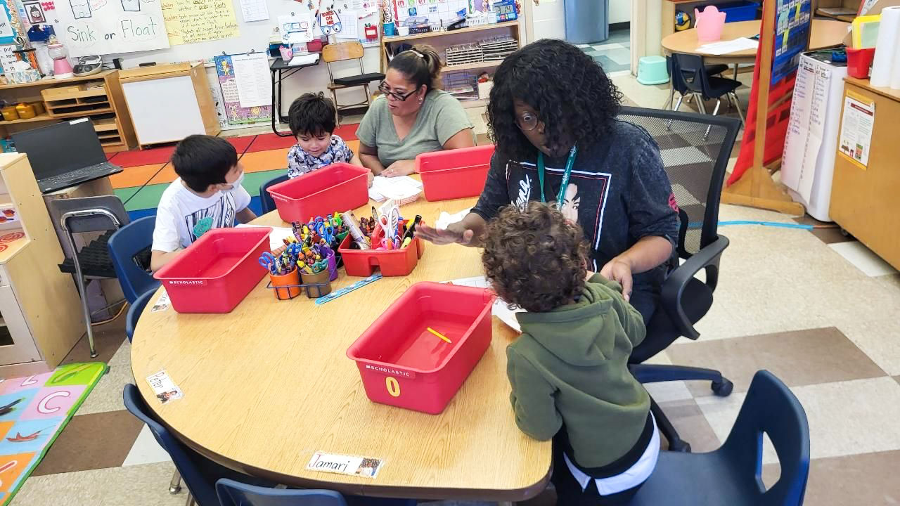 Kindergarteners work with two teachers around a circle table